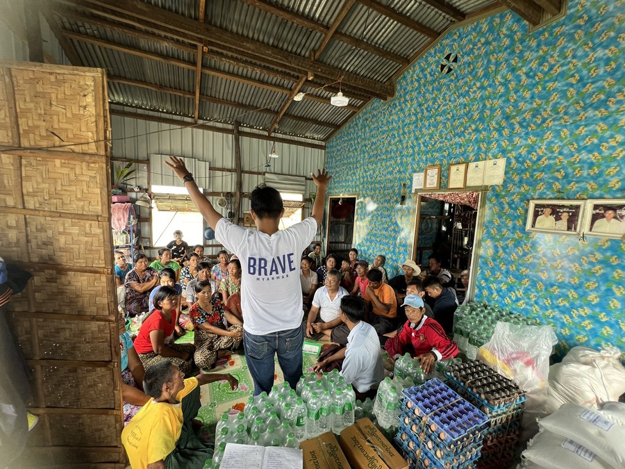BRAVE volunteer speaking to a seated crowd surrounded by water bottles and egg trays